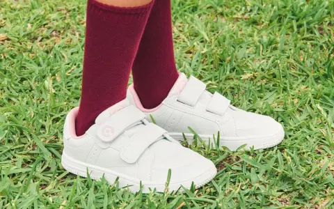 Niño con calcetines granates y zapatillas blancas con velcro, listas para limpiar y jugar en el césped.