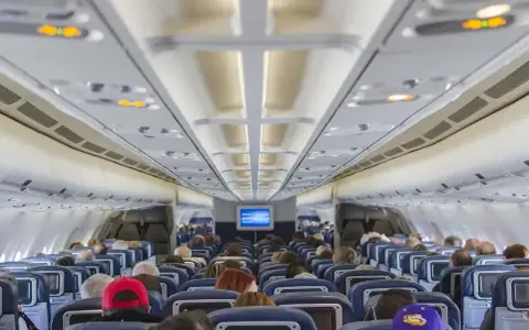 Wnętrze samolotu Boeing 737 Ryanair. Pasażerowie siedzą w rzędach niebieskich foteli, patrząc w stronę kokpitu.
