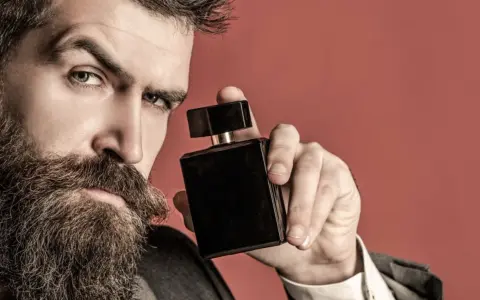 Mężczyzna z brodą trzyma czarne perfumy. Zastanawia się, gdzie psikać perfumy męskie, by zapach był subtelny i uwodzicielski.