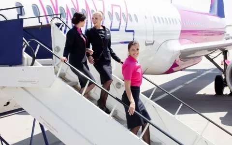 Uśmiechnięte stewardessy Wizz Air schodzą po schodkach. Ciekawe, ile zarabia stewardessa Wizz Air za taką pracę?