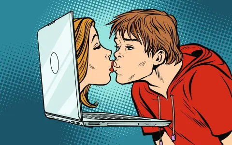 Chłopak i dziewczyna całują się przez ekran laptopa, symbolizując cyber sex i wirtualną bliskość.