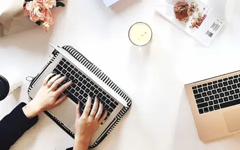 Kobieta pisze na laptopie, przygotowując wypowiedzenie umowy o dzieło. Obok świeca, muffinka i bukiet kwiatów.