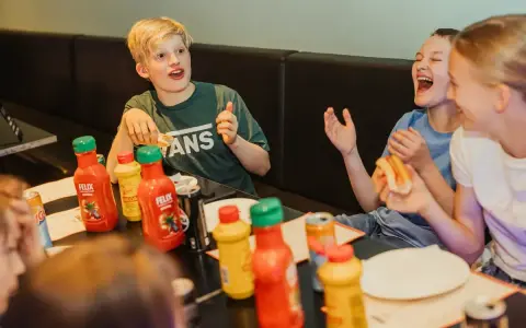 Barn skrattar och äter korv med bröd vid ett bord med Felix ketchup och senap. Perfekt för tips på femkamp!