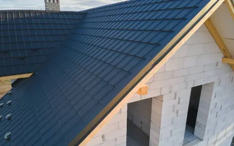 Nowy dach z ciemnogranatowej blachodachówki, wiatrownica zamontowana. Trwa obróbka dachu.