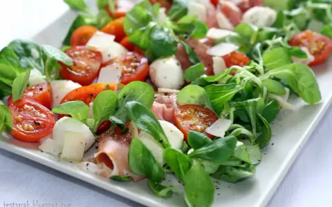 Pyszna sałatka z szynką parmeńską, pomidorkami koktajlowymi, mozzarellą i świeżą rukolą. Idealna na lekki posiłek.