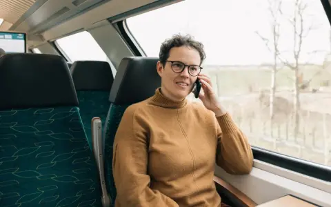 Kobieta w brązowym swetrze rozmawia przez telefon w pociągu. Czas na moją kolej, by usiąść przy oknie i podziwiać widoki.