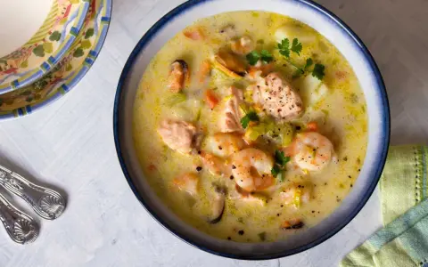 Sopa cremosa de pescado con salmón, gambas y mejillones, decorada con perejil.