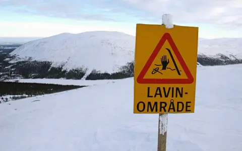 Varning för lavin vid Kebnekaise. Ett gult varningsskylt med en hand, skidor och rep i en röd triangel.