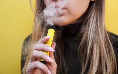Mujer exhala vapor de un vaper sin nicotina, pero ¿sabías que el vaper sin nicotina mancha los dientes?