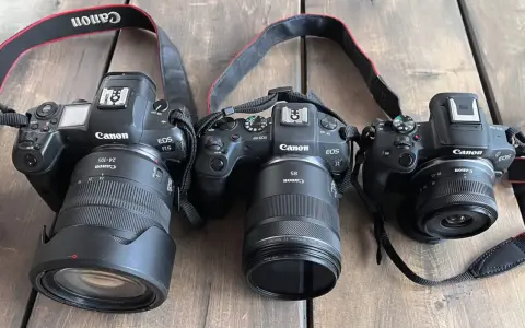 Trzy aparaty Canon EOS R, RP i R5 z obiektywami leżą obok siebie. Pełna klatka w całej okazałości.