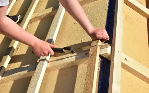 Holzfaserplatte Fassade: Hände sägen Holz für den Hausbau.