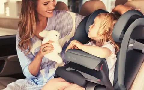 Uśmiechnięta mama z pluszowym zajączkiem przytula córkę w foteliku samochodowym Cybex Pallas 9-36 kg.