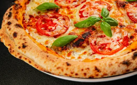 Pyszna pizza Margherita z pomidorami i bazylią, idealnie wypieczona w wysokiej temperaturze przez kilka minut.