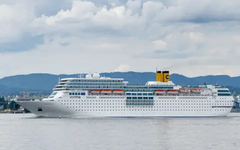 La nave da crociera Costa Romantica naviga in un mare calmo, con montagne verdi sullo sfondo.