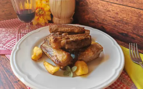 Succulente costine di maiale in padella, dorate e saporite, servite con patate arrosto e un rametto di salvia.