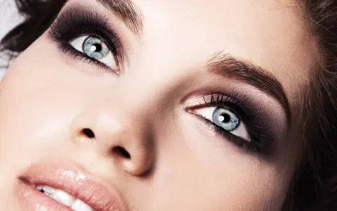 Occhi azzurri intensificati da un trucco smokey eyes audace, con labbra lucide e un accenno di sorriso.