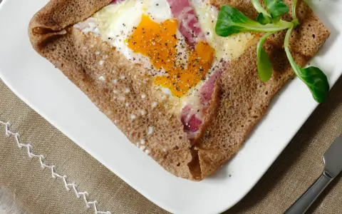 Une galette bretonne garnie d'un œuf, de jambon et de fromage, poivrée et décorée d'une feuille verte. Un délice de french crepes !