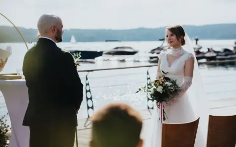 Panna młoda w białej sukni i pan młody w garniturze podczas ceremonii ślub rzymski nad jeziorem.