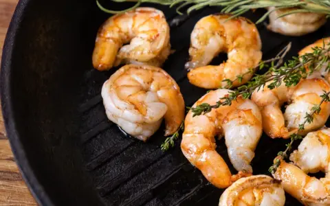 Gambas a la plancha jugosas y doradas, con ramitas de tomillo fresco sobre una sartén de hierro fundido.