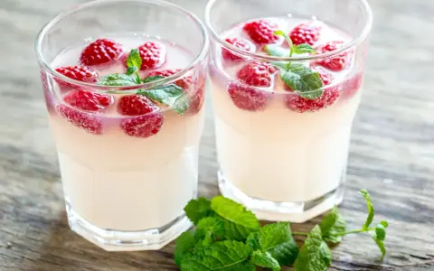Dwa orzeźwiające drinki z limoncello, malinami i miętą na drewnianym blacie. Idealne na letnie popołudnie.