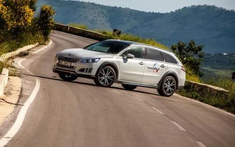 Białe kombi Peugeot 508 RXH na krętej drodze w górach.