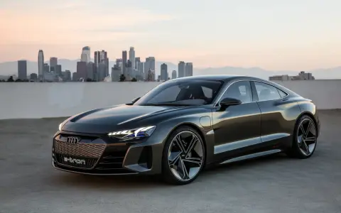 Ciemnoszary Audi e-tron GT stoi na tle panoramy miasta o zachodzie słońca.