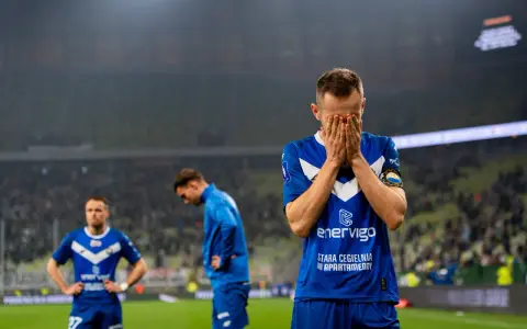 Piłkarz w niebieskiej koszulce z napisem "enerVigo" zakrywa twarz dłońmi. W tle inni zawodnicy i trybuny. Emocje po przegranym meczu w I lidze piłki ręcznej.