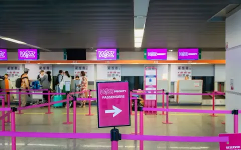 Kasa Wizz Air, gdzie pasażerowie dokonują self check-in. Różowe taśmy wyznaczają kolejkę do stanowisk odprawy.