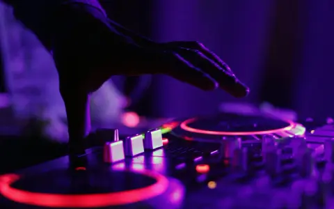 Dłoń DJ-a nad konsolą, czerwone i fioletowe światła. To właśnie tak tworzy się dubstep, co to za muzyka?