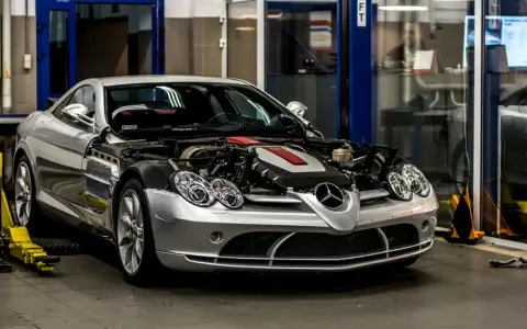 Srebrny Mercedes McLaren z otwartą maską, odsłaniającą potężny silnik, stoi w warsztacie.