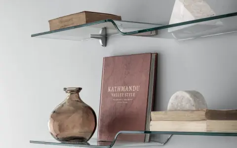 Idee mensole ingresso: vetro curvo con libri antichi, vaso ambrato e scultura in marmo.