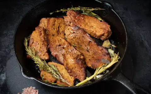 Seitan que es: trozos dorados y sabrosos de seitan cocinados en sartén con hierbas aromáticas como romero y tomillo.