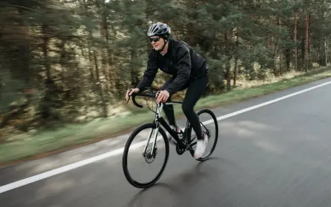Mężczyzna w kasku i okularach jedzie na rowerze szosowym przez las. To świetny sposób, jak schudnąć na rowerze, poprawiając kondycję.