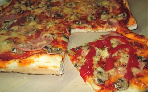 Pyszna pizza na cienkim cieście z pieczarkami i szynką, polana ketchupem. Idealna na szybki obiad.
