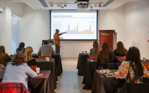 A presenter discusses market performance at Christie's, showing auction data to an audience.