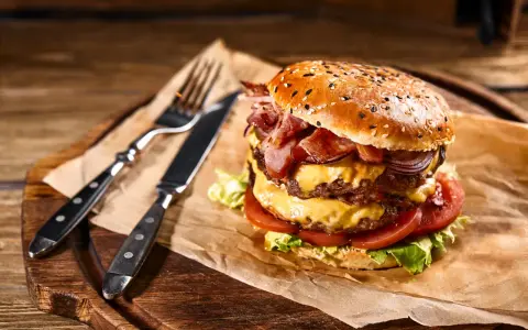 Soczysty burger z podwójną porcją mięsa, serem, bekonem i warzywami na desce z widelcem i nożem.