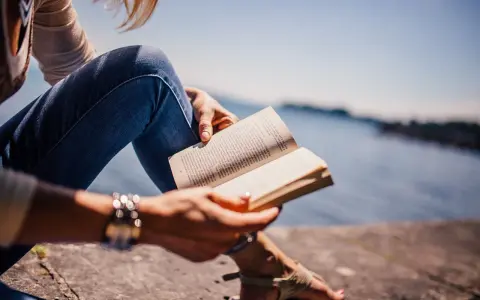 Persona sentada junto al agua, leyendo un libro en francés.