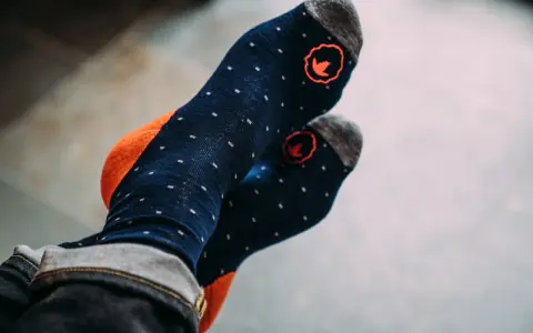 Blaue Socken mit orangen Akzenten und kleinen weißen Punkten. Die Socken haben ein rotes Logo und sind aus Merinowolle, ideal zum Waschen.
