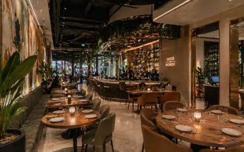 Elegantes mesas y un bar iluminado, con arte mural y plantas, ofrecen **ideas decoración restaurante** acogedoras.