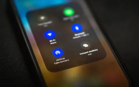 Ekran telefonu z widocznym menu, gdzie opcja AirDrop jest podświetlona. To funkcja do bezprzewodowego udostępniania plików między urządzeniami Apple.