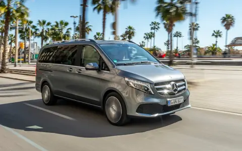 Szary Mercedes minivan jedzie ulicą w słoneczny dzień, otoczony palmami.