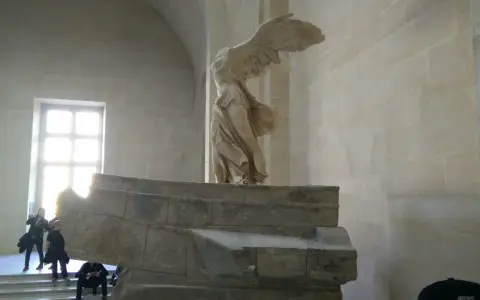 Skrzydlata Nike, symbol zwycięstwa, niczym mit, unosi się nad kamiennym postumentem.