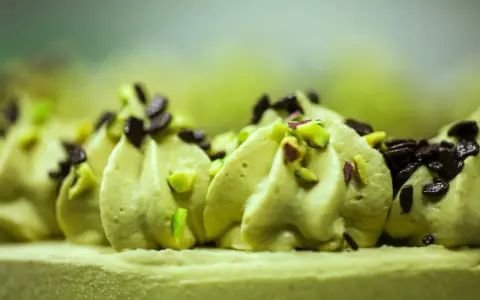 Delikatna masa pistacjowa ozdobiona kawałkami pistacji i czekolady, tworząca apetyczny deser.