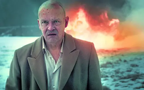 Jan Frycz w dramatycznej scenie, jak z najlepszych filmów i seriali. W tle płomienie, na głowie ślady walki.