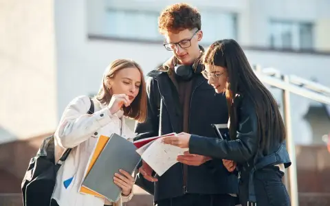 Trzech studentów dyskutuje nad notatkami, ich status ucznia widoczny w skupieniu i materiałach.
