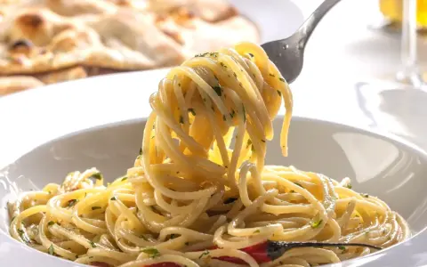 Pyszne dania z makaronem: spaghetti z ziołami i czosnkiem, na talerzu, z widocznym w tle pieczywem.