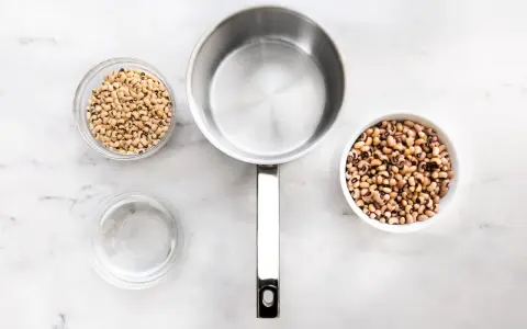 Vorbereitung zum Bohne kochen: zwei Schüsseln mit Schwarzaugenbohnen, ein Topf und eine Schüssel Wasser auf Marmoruntergrund.