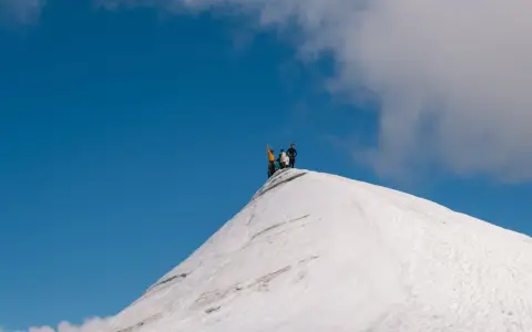 Vandrare på toppen av en snötäckt bergstopp, en vy som ger en känsla av var ligger Kebnekaise.
