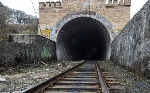 Torowisko prowadzi do ciemnego tunelu pod ceglanym łukiem z blankami, przypominającym bramę do dawnej kopalni Rydułtowy.