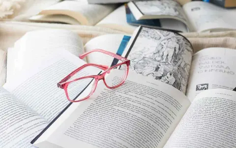 Różowe okulary spoczywają na otwartych książkach, tworząc atmosferę nauki i wiedzy. ibidem.